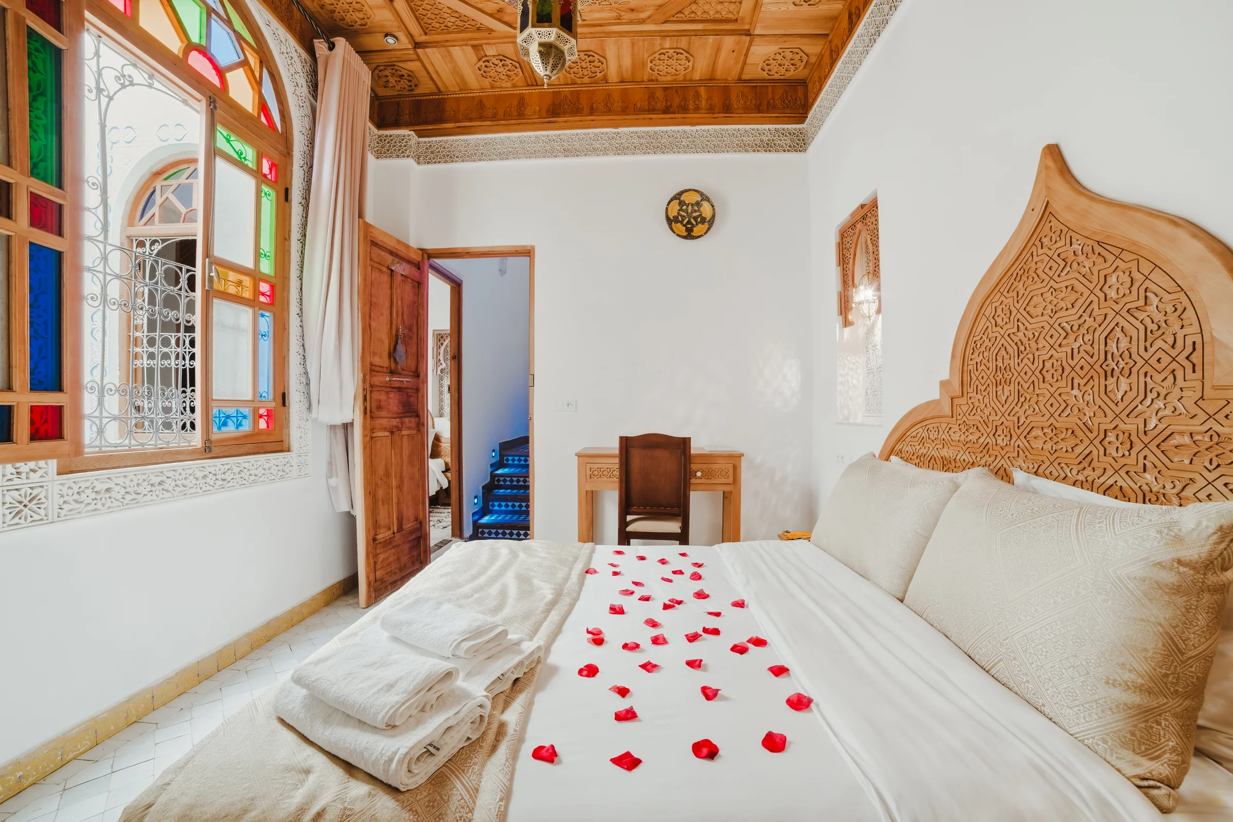 Bed with rose petals beside a colourful window in a riad
